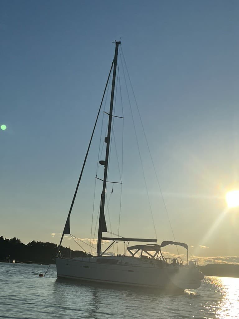 Seilbåten Evita i silhuett mot solen ved solnedgang, med masten godt synlig mot himmelen.